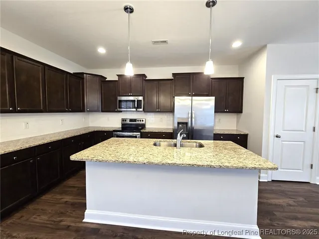 a kitchen with kitchen island granite countertop a stove a sink a center island a refrigerator and cabinets
