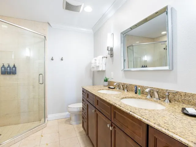 a bathroom with a granite countertop sink a toilet a mirror and shower