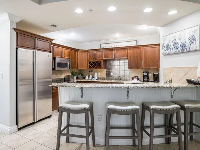 a kitchen with stainless steel appliances granite countertop a dining table chairs refrigerator and sink