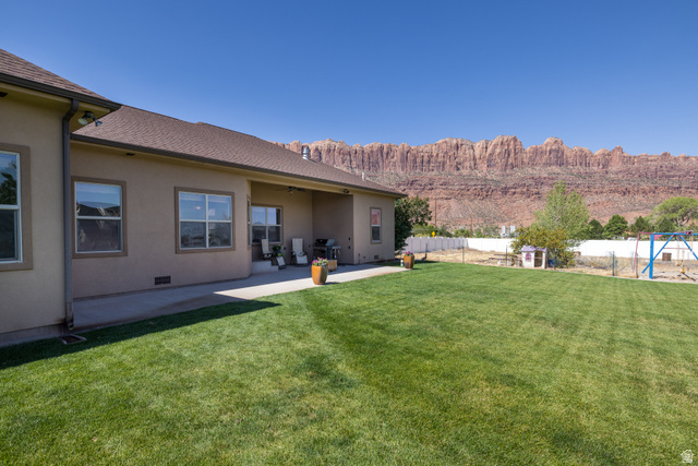 4635 East Sunny Acres Lane Moab, UT 84532 - Photo 21 of 56 Expansive green lawn with a concrete patio under a stucco exterior, featuring multiple windows and a mountain backdrop