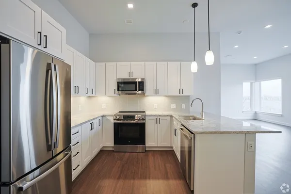 a kitchen with stainless steel appliances granite countertop a refrigerator a sink dishwasher a stove and white cabinets with wooden floor