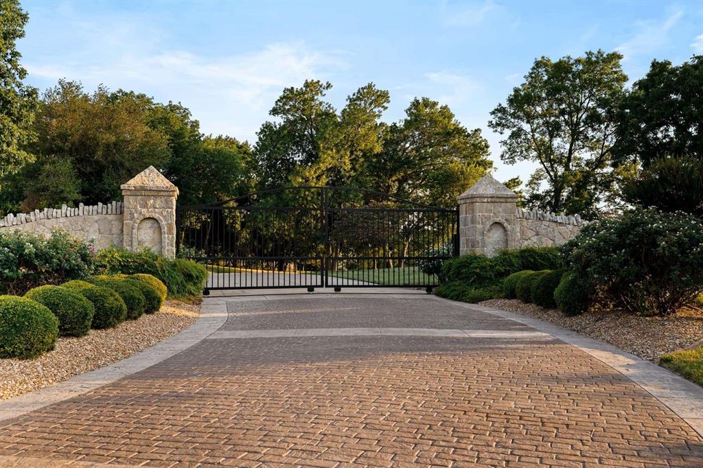 2115 Paradise Rnch Trail McKinney, TX 75071 - Photo 37 of 40 Gated entry featuring a brick paver driveway, stone pillars, wrought iron gates, and perimeter stone walls with lush landscaping