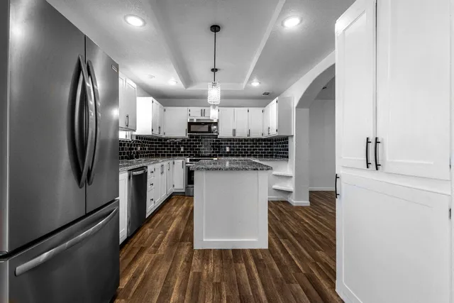 a view of an empty room and kitchen with wooden floor