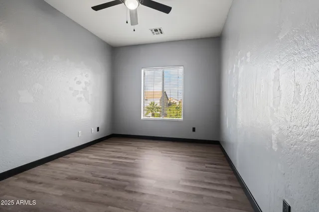 an empty room with wooden floor chandelier fan and windows