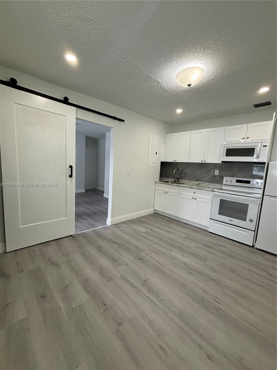 an empty room with wooden floor kitchen view and windows
