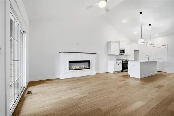 a view of an empty room with kitchen and fireplace