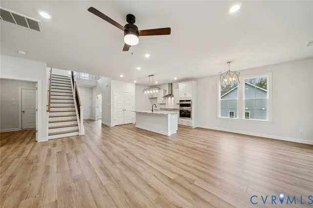an empty room with wooden floor staircase and windows