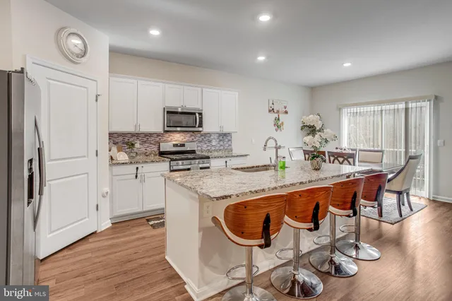 a kitchen with stainless steel appliances granite countertop a stove top oven a refrigerator a sink and a dining table with wooden floor