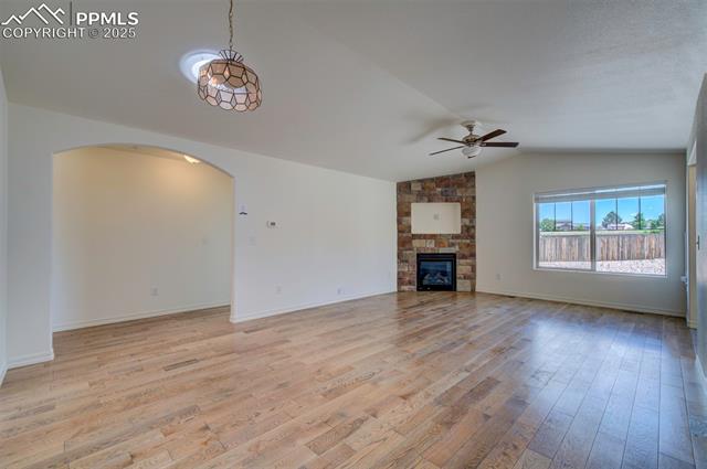 6604 Watusi Road Peyton, CO 80831 - Photo 7 of 40 Unfurnished living room with a ceiling fan, arched walkways, light wood-style flooring, vaulted ceiling, and a fireplace