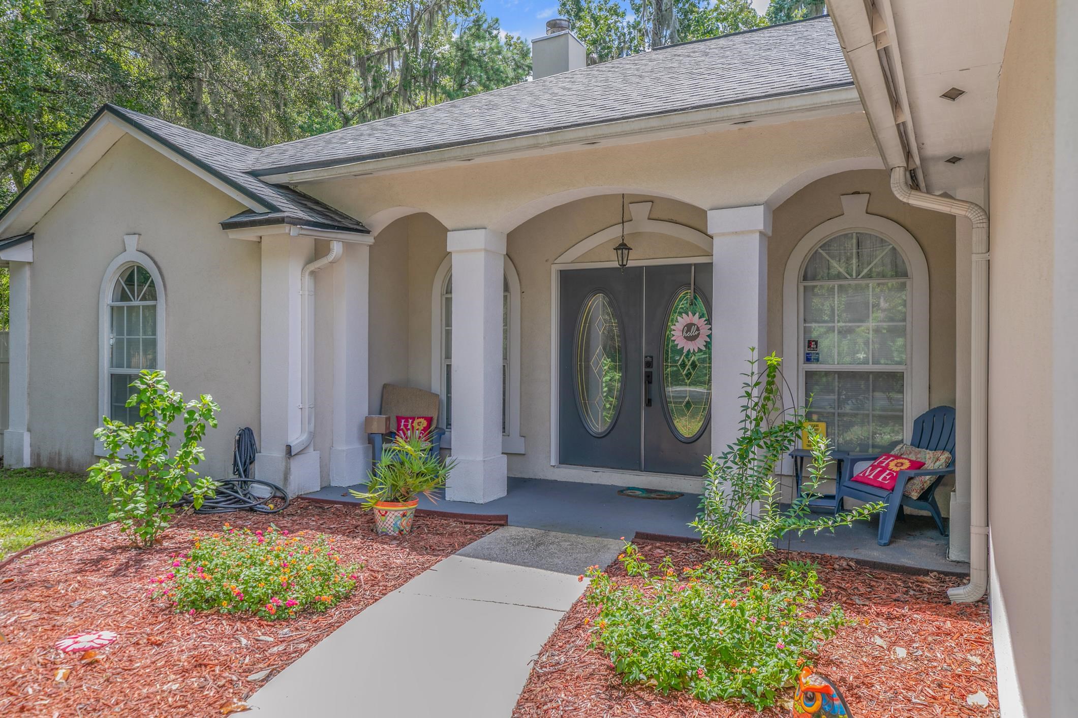 Doorway to property with a chimney, covered porch, stucco siding, and roof with shingles