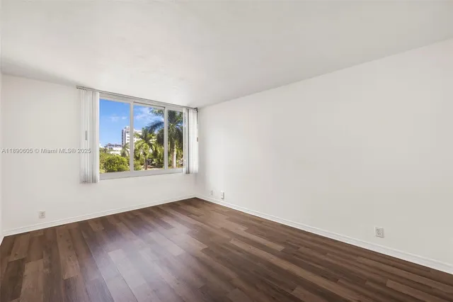 a view of an empty room with wooden floor and window