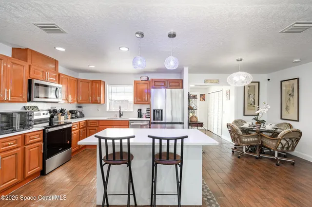 a kitchen with stainless steel appliances granite countertop a stove top oven a sink dishwasher a dining table and chairs with wooden floor