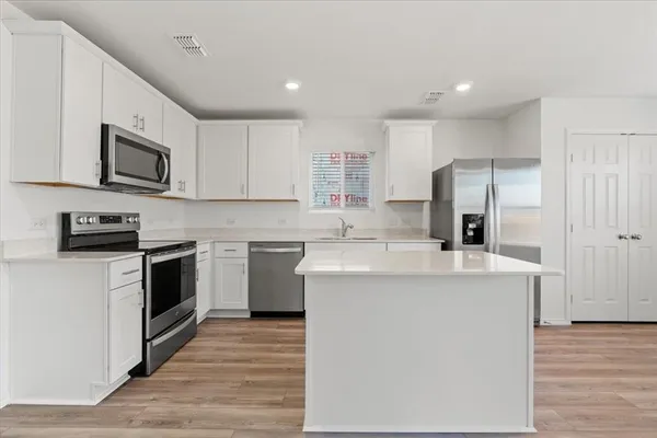 a kitchen with stainless steel appliances a stove top oven a sink a refrigerator white cabinets and wooden floor