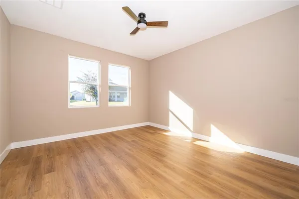 an empty room with wooden floor ceiling fan and windows