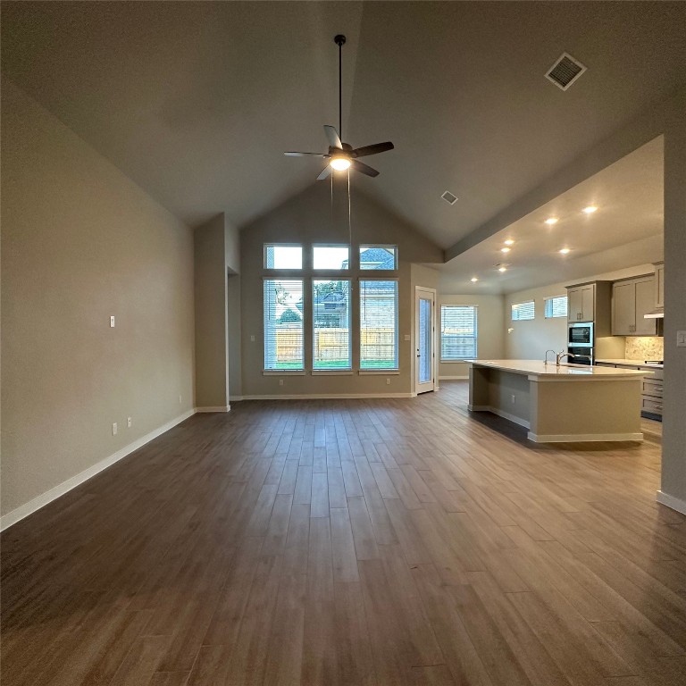 a view of an empty room with wooden floor and a kitchen