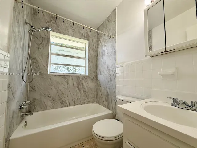 a bathroom with a granite countertop bathtub shower sink vanity and toilet