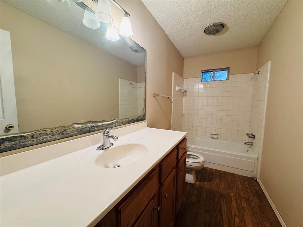 721 Mackey Ranch Road Bruceville-Eddy, TX 76524 - Photo 12 of 33 Vanity with integrated sink, wood-finish flooring, white tiled shower surround, recessed window, and wall-mounted light fixture