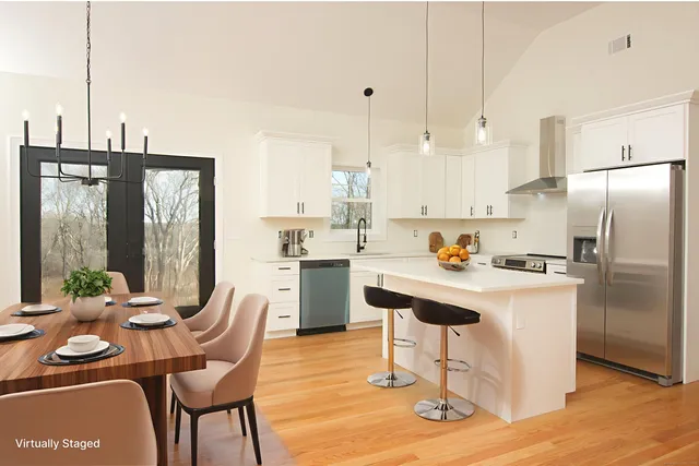 a kitchen with stainless steel appliances kitchen island granite countertop a dining table chairs and a refrigerator