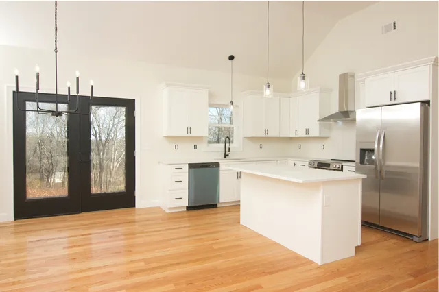 a kitchen with stainless steel appliances granite countertop a refrigerator a sink dishwasher a stove and white cabinets with wooden floor