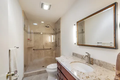 a bathroom with a granite countertop sink a mirror a shower and a toilet
