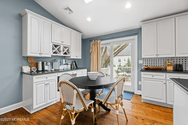 a kitchen with stainless steel appliances granite countertop a stove a refrigerator a sink and white cabinets with wooden floor
