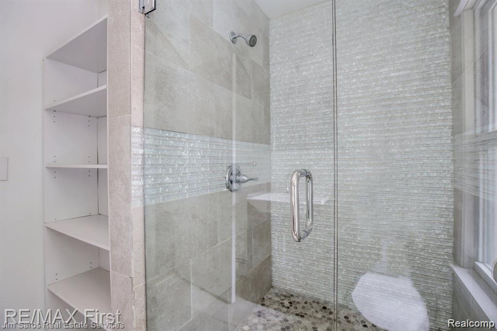 1349 Devonshire Road Grosse Pointe, MI 48230 - Photo 19 of 26 Walk-in shower featuring a glass enclosure, pebble-tile flooring, and large format wall tiles with a decorative mosaic band