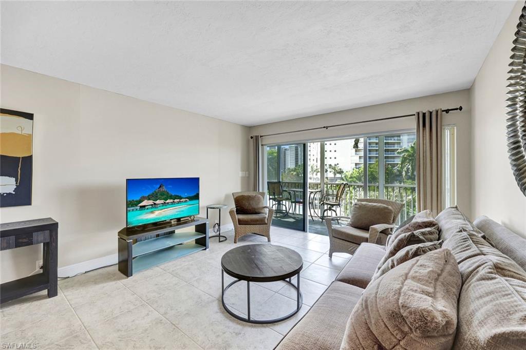 1 Bluebill Avenue, Unit 409 Naples, FL 34108 - Photo 2 of 25 a living room with furniture a floor to ceiling window and a flat screen tv