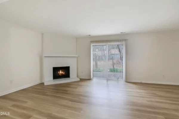 a view of an empty room with wooden floor and a fireplace