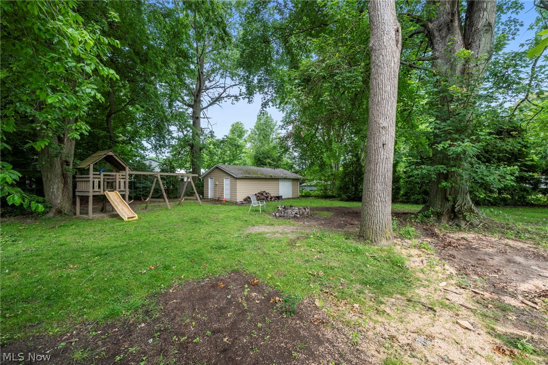 6472 Southgrove Road Mentor, OH 44060 - Photo 35 of 37 Spacious backyard featuring extensive green space, mature trees, a detached storage shed with siding, and a designated fire pit area