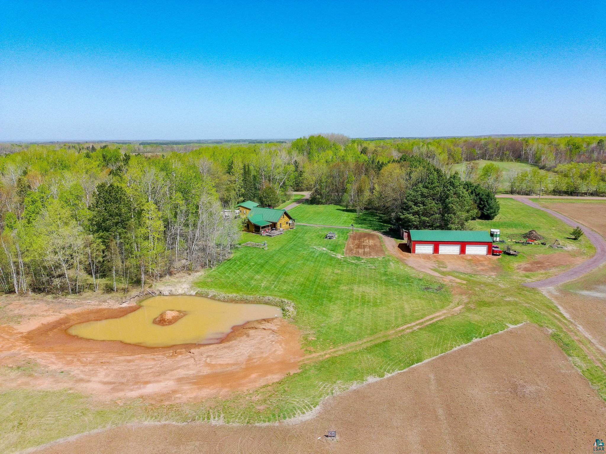 37590 Degerstrom Road Askov, MN 55704 - Photo 5 of 53 Expansive property featuring a log cabin, a red outbuilding with three garage doors, a private pond, vast green lawns, and surrounding wooded areas
