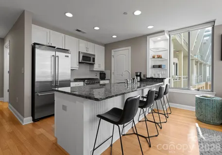 a kitchen with stainless steel appliances granite countertop a stove a refrigerator a sink a dining table and chairs with wooden floor