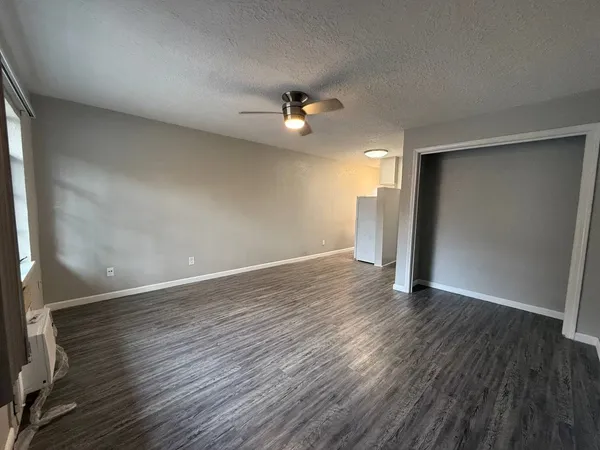 an empty room with wooden floor ceiling fan and window