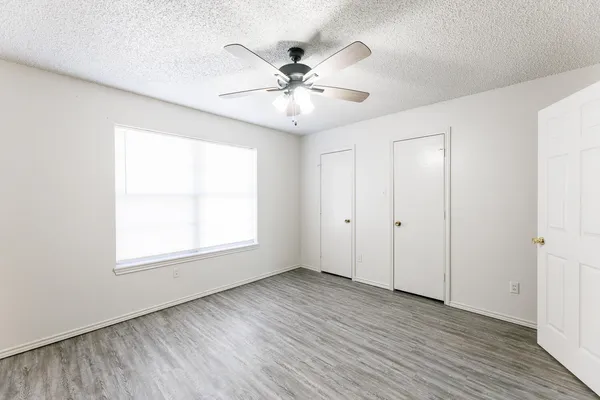 an empty room with wooden floor fan and windows