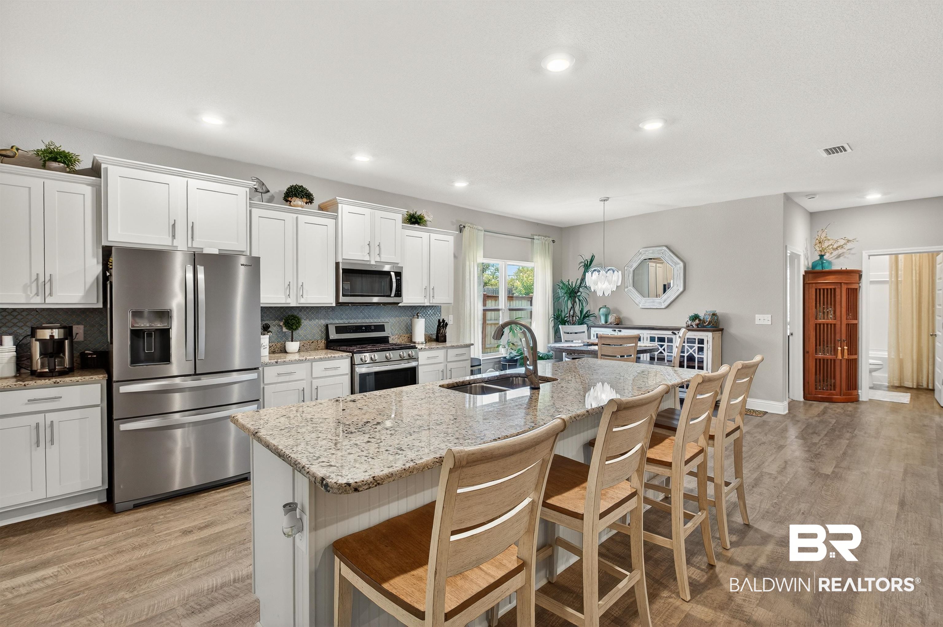 8735 Bronze Lane Foley, AL 36535 - Photo 9 of 58 Kitchen featuring an expansive island with granite countertops, stainless steel appliances, white cabinetry, a tile backsplash, and wood-finish flooring