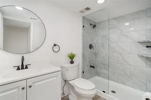 a bathroom with a toilet a sink a glass door a shower and mirror