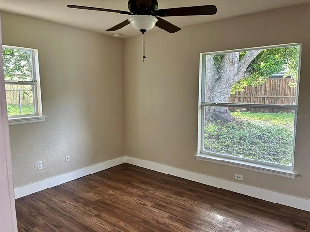 an empty room with wooden floor fan and windows