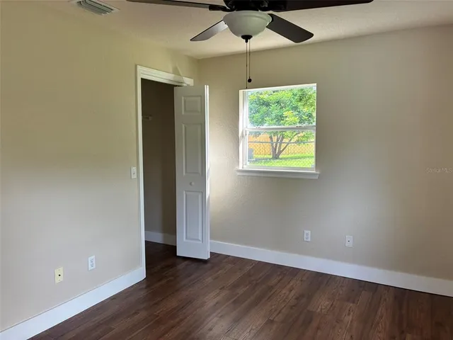 an empty room with wooden floor chandelier fan and windows