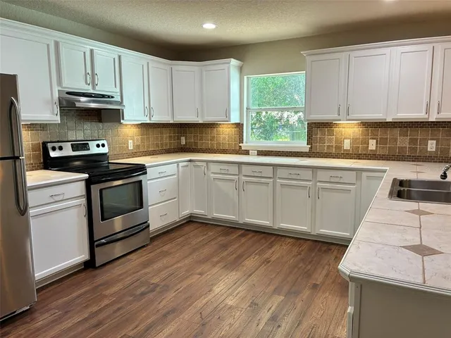 a kitchen with stainless steel appliances granite countertop a stove a sink and white cabinets