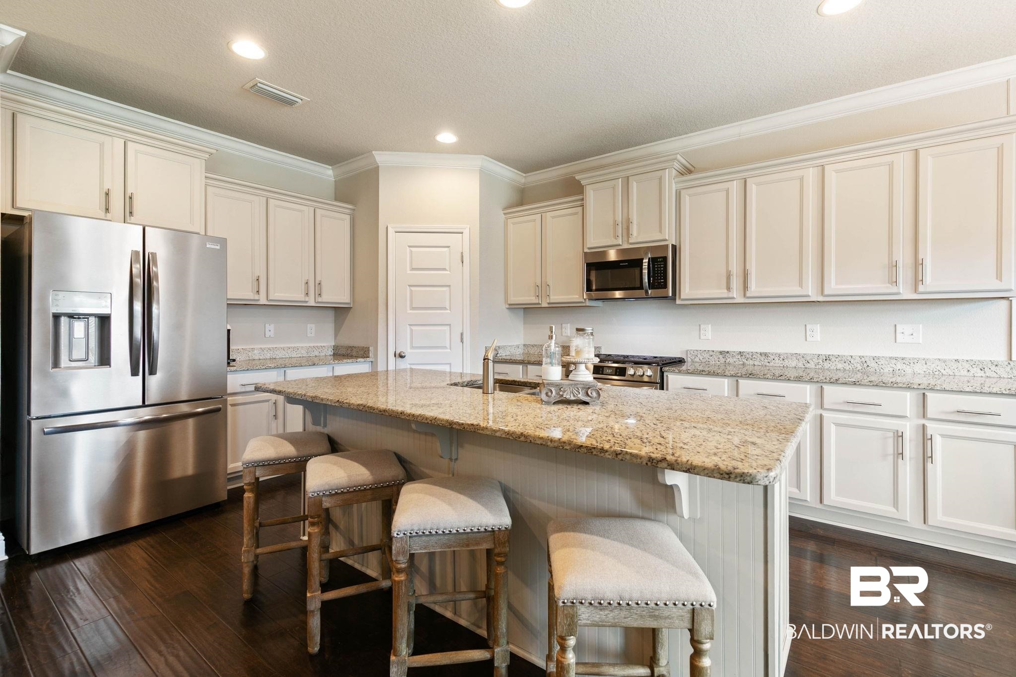 31187 Spoonbill Road Daphne, AL 36527 - Photo 13 of 85 Gourmet kitchen with a large central island, light-toned granite countertops, extensive white cabinetry, stainless steel appliances, and dark wood-finish flooring
