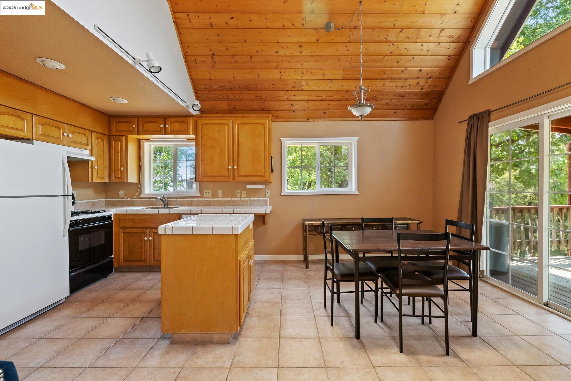 14799 Big Hill Road Sonora, CA 95370 - Photo 39 of 60 Kitchen featuring tile countertops, freestanding refrigerator, healthy amount of natural light, brown cabinetry, and vaulted ceiling