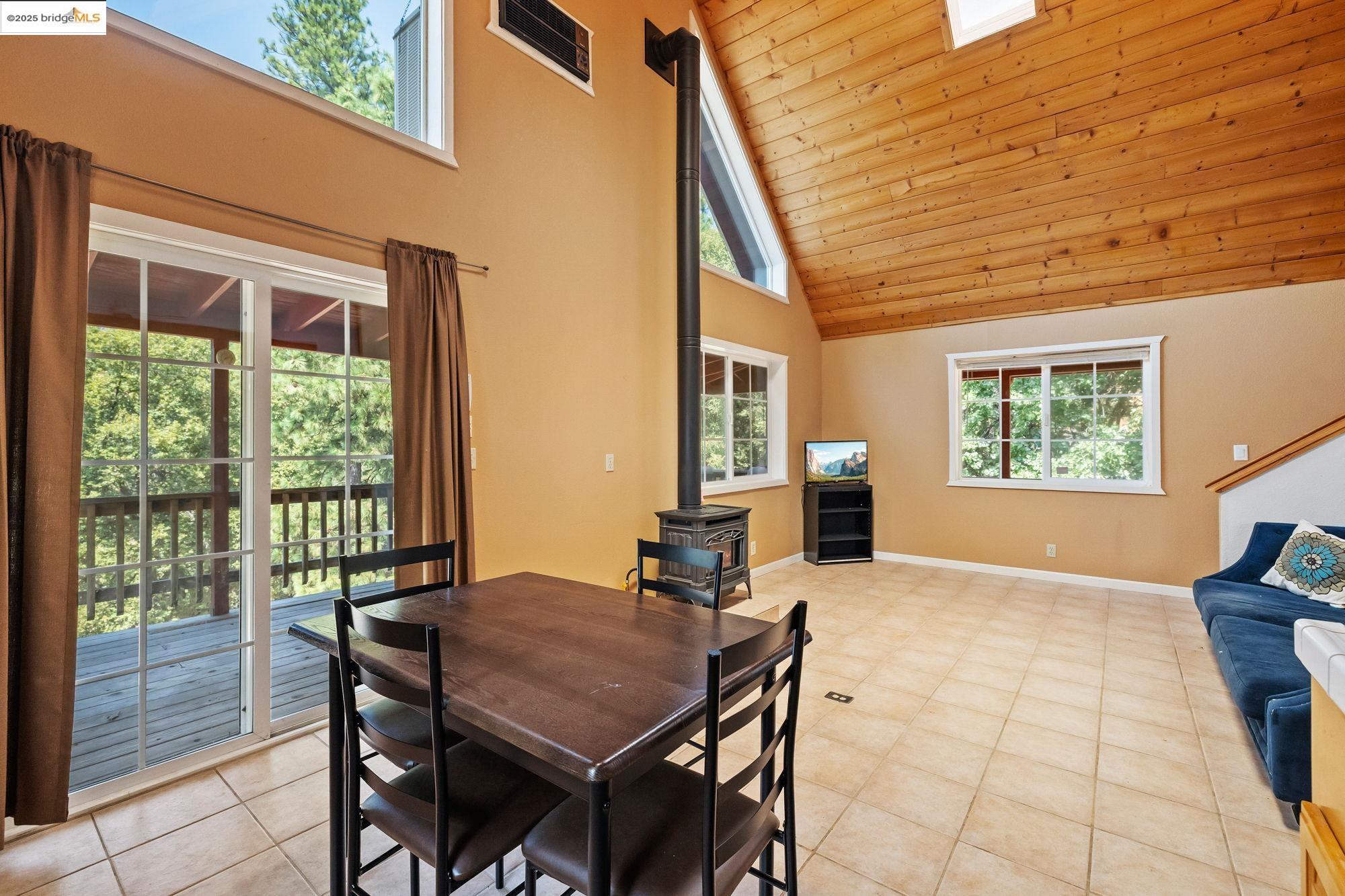 14799 Big Hill Road Sonora, CA 95370 - Photo 44 of 60 Dining area featuring a wood stove, high vaulted ceiling, wooden ceiling, and light tile patterned flooring