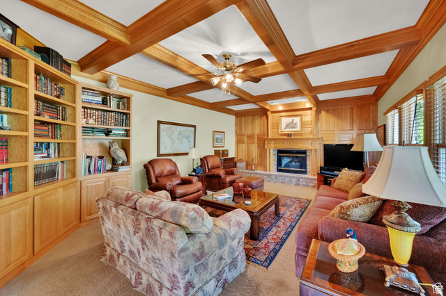 7740 Keswick Road Sandy, UT 84093 - Photo 23 of 74 Living area featuring a coffered wood-finish ceiling with a ceiling fan, a fireplace with a stone hearth and wood-paneled surround, and integrated wood-finish shelving with built-in cabinetry