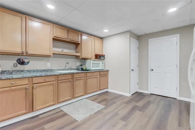 a view of an empty room and kitchen with wooden floor