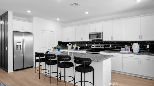 a kitchen with stainless steel appliances granite countertop a sink a stove a refrigerator and white cabinets