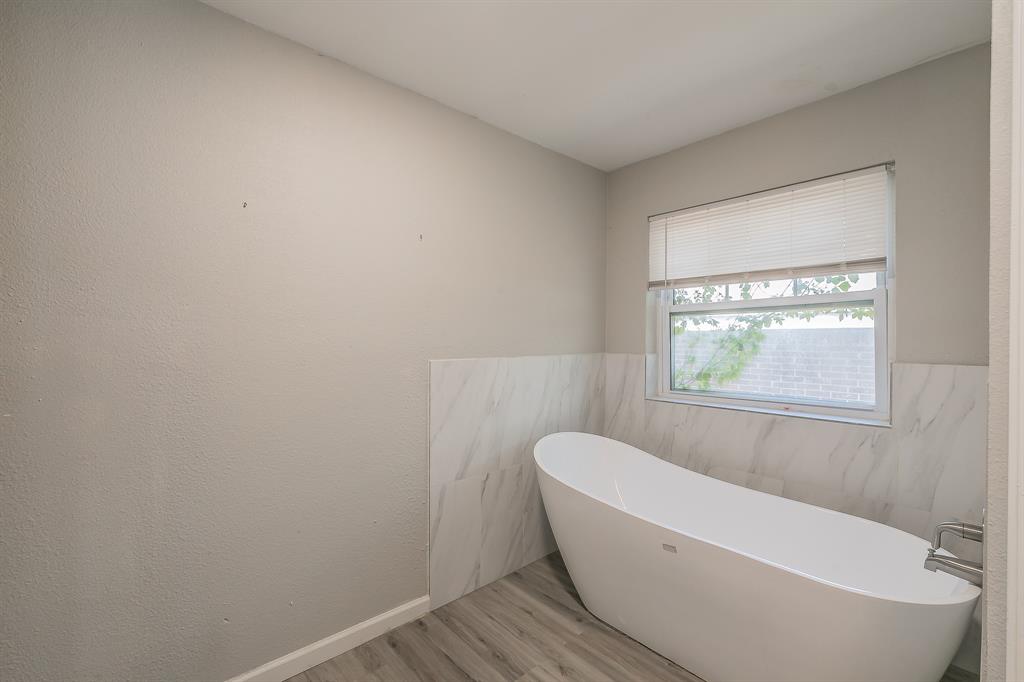 3025 David Drive Rowlett, TX 75088 - Photo 20 of 23 Full bathroom with wood finished floors, a freestanding tub, tile walls, and wainscoting