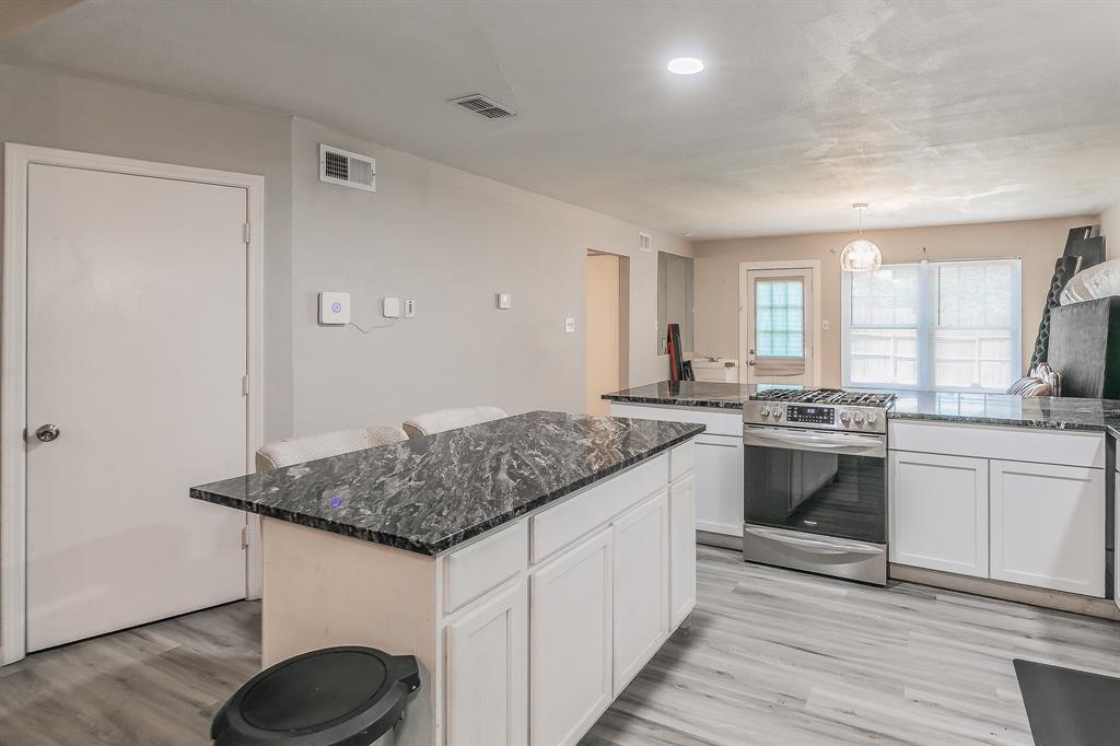 3025 David Drive Rowlett, TX 75088 - Photo 7 of 23 Kitchen with stainless steel range with gas stovetop, light wood finished floors, white cabinetry, a kitchen island, and dark stone countertops