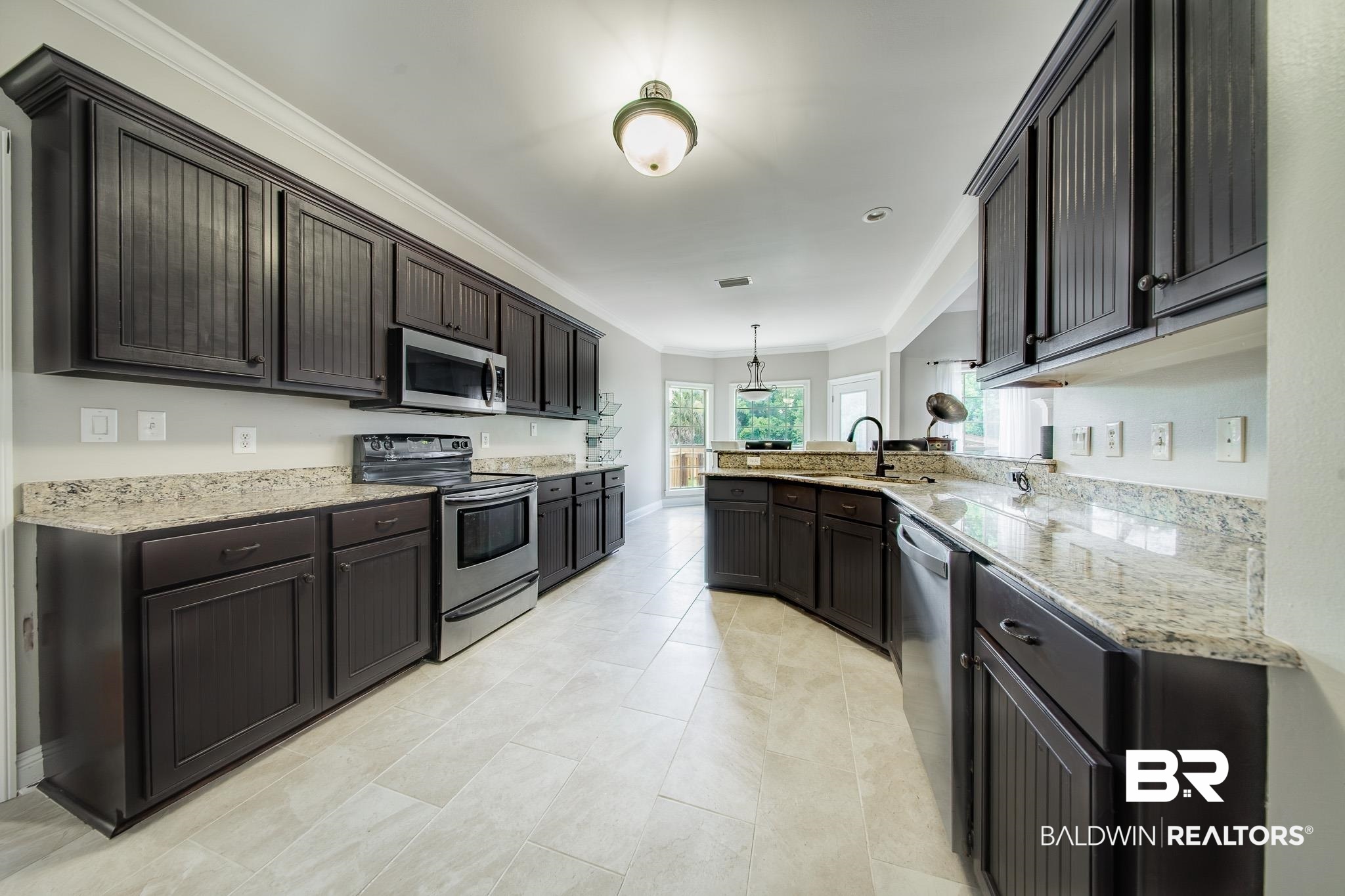8421 Weatherford Court Daphne, AL 36527 - Photo 12 of 36 Kitchen with stainless steel appliances, a peninsula, ornamental molding, light stone counters, and dark brown cabinetry