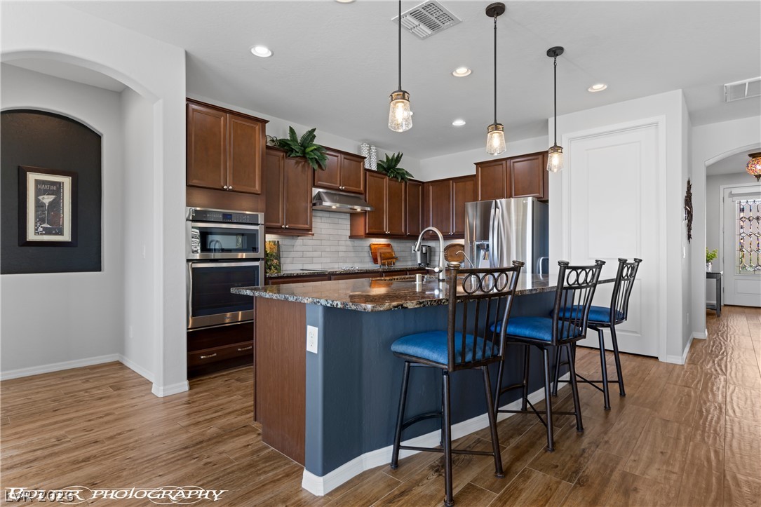 1262 Serenity Ridge Court Mesquite, NV 89034 - Photo 43 of 74 Kitchen with arched walkways, a kitchen bar, dark stone counters, a kitchen island with sink, and dark wood-style floors