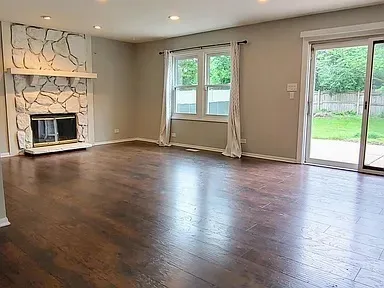 an empty room with wooden floor fireplace and windows