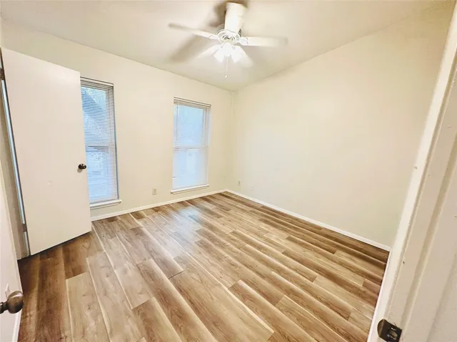 an empty room with wooden floor fan and windows